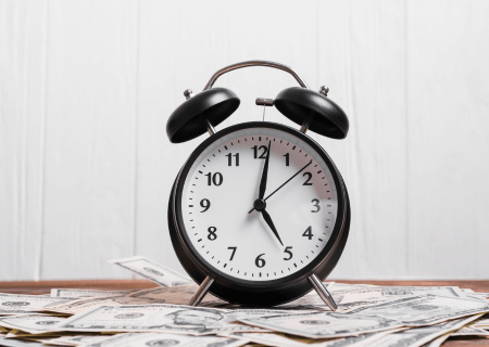 Notas de dinheiro sobre mesa e relógio em cima, em alusão ao controle de horas extras - Imagem de Freepik