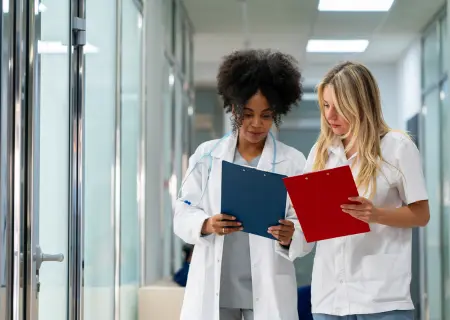 Duas médicas em corredor de hospital olhando suas pranchetas e conversando durante troca de turnos de trabalho - Imagem de Freepik