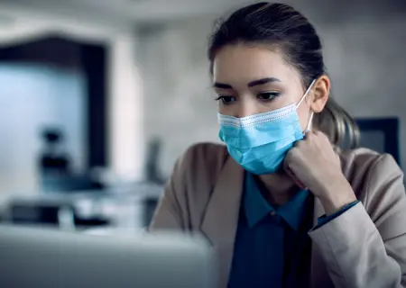 Trabalhadora mexendo em computador de máscara solicitando ausência por atestado médico - Imagem de Freepik