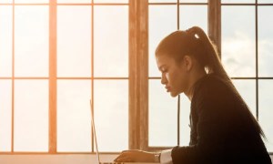 Trabalhadora mexendo em laptop na frente da janela no pôr do sol - Imagem de Freepik